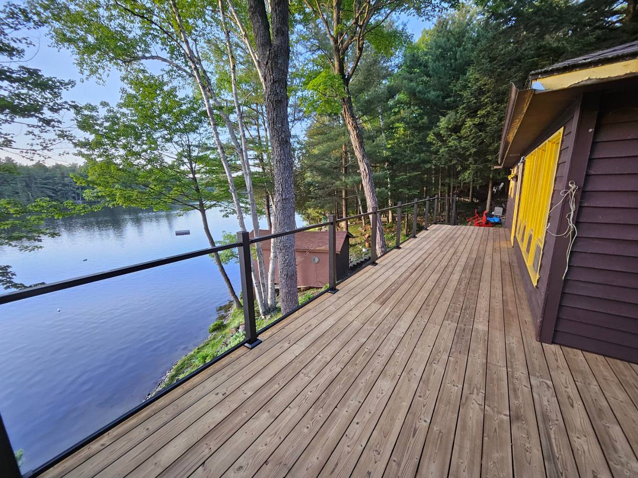 Terrasse en bois traité avec rampe en verre donnant sur l’eau près de Chambly